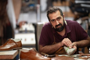 Yetenekli bir ayakkabıcı deri atölyesinde çalışıyor, ölçü bandı ve aletlerle kahverengi bir ayakkabı şekillendiriyor. Sıcak, odaklı sahne, işçilik, el yapımı ayakkabılar ve sanatsal gurur..