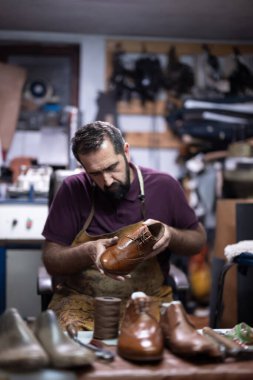 Meşgul bir atölye çalışmasında yetenekli bir zanaatkar diğer ayakkabı ve aletlerle çevrili kahverengi deri bir ayakkabı yapar. Sahne zanaat, sabır ve geleneksel ayakkabı yapma sanatını ön plana çıkarıyor.