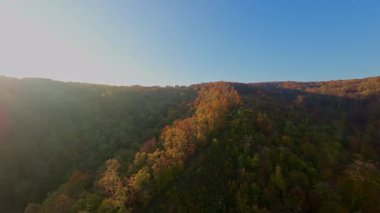 Canlı bir sonbahar ormanı boyunca manzaralı bir dağ bisikletli patikada heyecan verici bir yolculuk, berrak mavi gökyüzünün altındaki uzak şehrin nefes kesen panoramik manzarasıyla son buluyor..