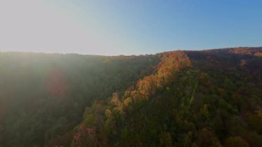 Canlı bir sonbahar ormanı boyunca manzaralı bir dağ bisikletli patikada heyecan verici bir yolculuk, berrak mavi gökyüzünün altındaki uzak şehrin nefes kesen panoramik manzarasıyla son buluyor..