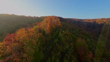 Canlı bir sonbahar ormanı boyunca manzaralı bir dağ bisikletli patikada heyecan verici bir yolculuk, berrak mavi gökyüzünün altındaki uzak şehrin nefes kesen panoramik manzarasıyla son buluyor..
