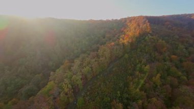 Canlı bir sonbahar ormanı boyunca manzaralı bir dağ bisikletli patikada heyecan verici bir yolculuk, berrak mavi gökyüzünün altındaki uzak şehrin nefes kesen panoramik manzarasıyla son buluyor..