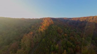 Canlı bir sonbahar ormanı boyunca manzaralı bir dağ bisikletli patikada heyecan verici bir yolculuk, berrak mavi gökyüzünün altındaki uzak şehrin nefes kesen panoramik manzarasıyla son buluyor..