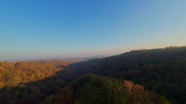 Canlı bir sonbahar ormanı boyunca manzaralı bir dağ bisikletli patikada heyecan verici bir yolculuk, berrak mavi gökyüzünün altındaki uzak şehrin nefes kesen panoramik manzarasıyla son buluyor..