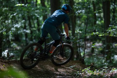 Dağ bisikleti süren bir bisikletçi sık bir orman patikasında miğfer ve koruyucu giysiler giyerek dolaşır. Güneş ışığı ağaçların arasından süzülür. Sürücü ormandan inerken, macerayı yakalar ve...