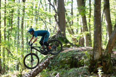Mavi dişli odaklanmış bir sürücü orman yolunda ahşap bir kütük köprü müzakere, açık hava macera, denge ve atletizm yakalamak parlak, yapraklı çevrede.