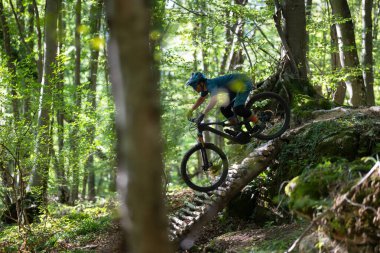 Kask takan bir bisikletçi yemyeşil bir ormanda ahşap bir rampada geziniyor denge, hız ve yeşil yaprakların ortasındaki elektrikli dağ bisikletine odaklanıyor..