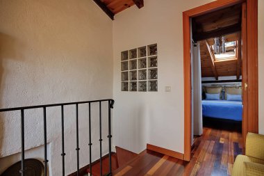 Ilık ahşap döşemeleri, metal korkulukları ve eğimli ahşap tavanın altında mavi yatak odasının kapısı olan güneşli bir çatı katı. Cam bloklar ve tavan penceresi ışık ve cazibe ekler.