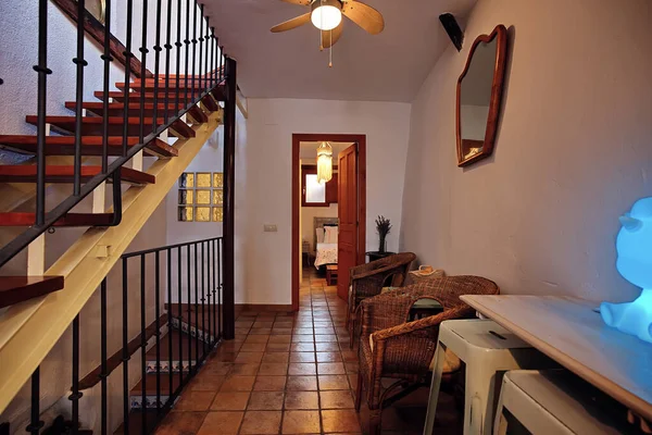 Sıcak, taşralı bir koridor içinde ahşap bir merdiven, hasır koltuklar, fayanslı döşemeler ve sıcak, davetkar bir ev atmosferi yaratan mavi bir lamba..