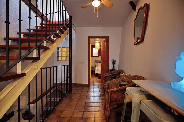 Sıcak, davetkar bir koridorda ahşap bir merdiven, terracotta fayansları, hasır koltuklar ve dekoratif bir ayna bulunur. Yumuşak ışık, kırsal bir aile evinde rahat bir atmosfer yaratır..