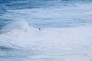 Yalnız bir sörfçü, engin mavi okyanus çevresini saran beyaz köpüğü oyarak, yüksek bir dalga boyunca süzülür. Spor ve doğa odaklı enerjik, maceracı bir ruh hali..