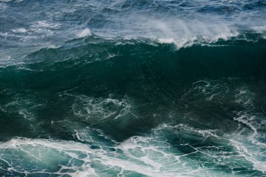 Büyük bir okyanus dalgasının güçlü bir yakın çekimi yuvarlanıyor ve kırılıyor, zengin mavileri, turkuaz suları ve beyaz spreyi ortaya çıkarıyor. Doğa, seyahat ve sörf temaları için ideal.