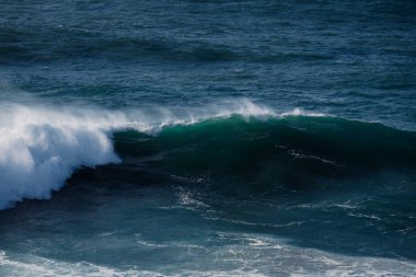 Güçlü bir okyanus dalgası koyu mavi bir denize doğru kıvrılır, tepede beyaz bir sprey. Doğa, seyahat ya da sahil temalı dramatik görüntüler gerektiren projeler için mükemmel..