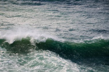 Yukarıdan çekilen dinamik bir deniz manzarası kıvrımlı yeşil dalgaları, beyaz köpüğü ve dokulu mavi suyu gösteriyor. Stok tahsilatlarında doğa, seyahat ve çevre temaları için ideal.