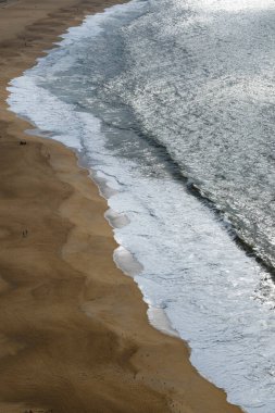 Altın kumun köpüklü dalgalarla ve parıldayan suyla buluştuğu uzun ve eğri bir kıyı şeridine kuşbakışı bir bakış açısı..