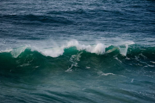 Beyaz köpüklü kıvrımlı bir turkuaz dalganın yakın görüntüsü, derin mavi arka plan, ve hareket eden su dokusu enerji, hareket ve denizin ham gücü..