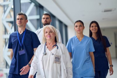 Bir grup sağlık uzmanı, gün ortasında hasta bakımına adanmışlık ve takım çalışması sergileyen modern bir hastane koridorunda güvenle ilerliyorlar..