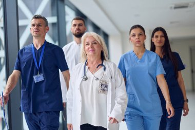 Aralarında doktor ve hemşirelerin de bulunduğu bir grup sağlık uzmanı, kasıtlı olarak parlak ve ferah bir hastane koridorunda yürüyor..