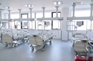Parlak ve temiz hastane odasında yüksek teknolojili tıbbi ekipmanlı birden fazla boş hastane yatağı var. Geniş pencereler, bol miktarda doğal ışık sağlıyor ve misafirperver bir ortam yaratıyor..
