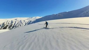 Tecrübeli bir kayakçı, heyecan verici bir serbest kayak macerası sırasında el değmemiş toz karı oyar. Açık mavi bir gökyüzünün altında, açık bir kışın aşırı ücra arazisinin tadını çıkarıyorum.