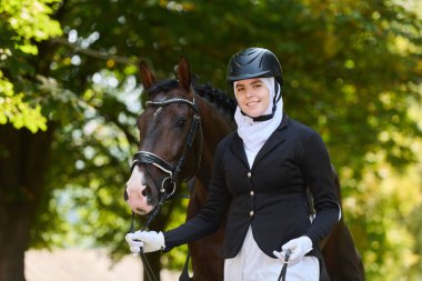Açık havada atıyla tesettürlü bir binicinin portresi. Gülümsüyor ve binici kaskı ve ceketi giyiyor. Bu görüntü binicilik sporlarını, yaşam tarzını ve...