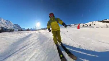 Dinamik bir kayak pistinin heyecanını yaşayın. Bir insan el değmemiş, karla kaplı bir dağı kazıyarak parlak bir güneşin ve açık mavi gökyüzünün altında güzel bir kar püskürtüsü püskürtür..