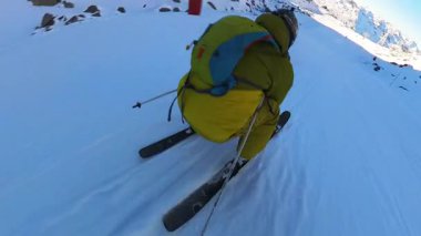 Sarı bir kayak takımı giymiş birinin güneşli bir dağ yamacına taze kar kazıyarak kış sporlarının heyecanını sergilediği keyifli yokuş aşağı yolculuğunu tecrübe edin..