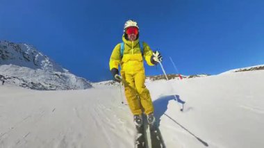 Canlı bir video, parlak sarı takım elbiseli bir kayakçıyı açık mavi bir gökyüzünün altında el değmemiş, karlı bir dağ yamacını oyarken yakalıyor..