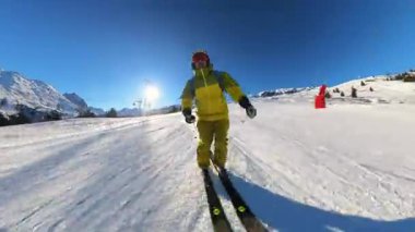 Dinamik bir kayak pistinin heyecanını yaşayın. Bir insan el değmemiş, karla kaplı bir dağı kazıyarak parlak bir güneşin ve açık mavi gökyüzünün altında güzel bir kar püskürtüsü püskürtür..