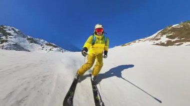 Aydınlık ve açık bir günde el değmemiş karlı bir dağda kayak yapmanın heyecanını yaşayın. Bir kayakçı döner, toz bulutları gönderir heybetli tepelere ve canlı mavi gökyüzüne.