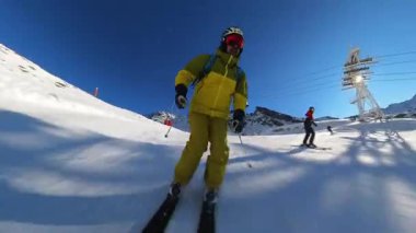 Güneşli bir kış gününün heyecanını bir kayakçının el değmemiş bir dağ yamacını oymasıyla yaşayın. Açık mavi gökyüzünün, taze karın ve kış sporlarının neşesini vurgulayan büyüleyici dağ manzarasının tadını çıkar.