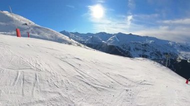 Resimli bir dağ yamacından inen kayakçıların ve snowboardcuların panoramik manzarasının tadını çıkarın. Gondol, baş döndürücü mavi bir gökyüzüne ve parlak bir güneşe karşı geçer ve kış sporunun özünü yakalar.