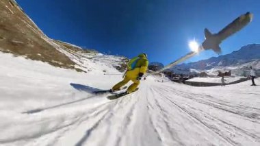 Kış sporlarının heyecanını bir kayakçının bakış açısıyla yaşayın el değmemiş, karlı bir dağ yamacında, berrak mavi gökyüzü altındaki pitoresk bir tatil köyünün önünden geçerken..