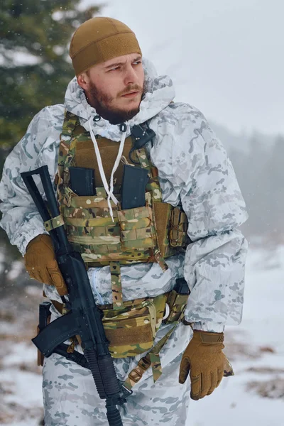 Karlı bir ormanda kar maskesi ve taktik taşıyıcı taşıyan silahlı asker, soğuk hava askeri eğitimi sırasında etrafı tararken tüfeğini kavrıyor.