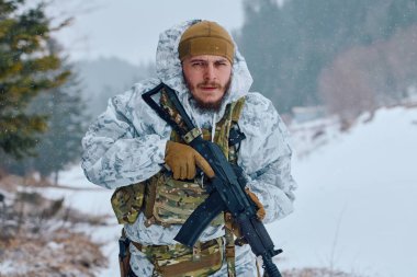 Beyaz kış kamuflajı ve taktik teçhizatı takan bir asker, karlı bir ormanda devriye gezerken bir saldırı tüfeği tutuyor ve hazırlık, dayanıklılık ve soğuk hava askeri operasyonlarını sürdürüyor..