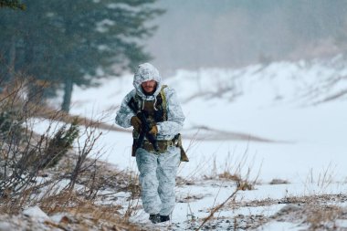Beyaz kış kamuflajı ve taktik teçhizatı giyen bir asker karlı bir orman sınırında devriye geziyor, soğuk, rüzgarlı koşullarda gizlenmeyi, dayanıklılığı ve askeri gücü ön plana çıkaran bir tüfeği kavrıyor.