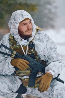 Beyaz kışlık kamuflaj ve taktik teçhizat giyen silahlı askerler kar altında diz çökerek, karlı ormanı tehdit için tararken bir tüfek tutuyorlar. Soğuk, odaklanmış, kış operasyonlarına hazır ve...