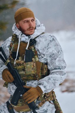 Beyaz kış kamuflajı ve taktiksel yelek giyen silahlı asker kar yağarken tetikte, karlı bir dağ manzarasını tararken veya soğuk hava askeri operasyonları sırasında tüfeği kavrıyor.