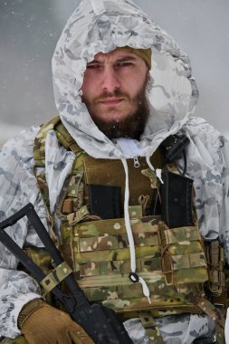 Kar maskesi ve taktik yelek giymiş, karlı bir arazide tüfek tutan bir askerin yakın plan portresi. Stoik ifade soğuk hava operasyonları sırasında odak, esneklik ve hazırlık iletir.