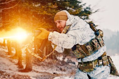 Beyaz kış kamuflajlı bir asker, karlı bir orman tatbikatı sırasında saldırı tüfeği ateşliyor. Soğuk hava koşullarında yoğun, odaklanma ve taktik hareket gösteriyor..