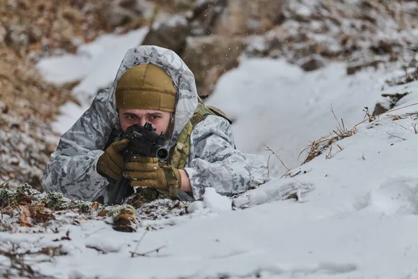 Beyaz kış kamuflajlı bir asker karlı bir orman çukurunda kar taneleri düşerken tüfeği doğrultuyor. Sahne gizlenmeyi, odaklanmayı, soğuk hava eğitimini ve askeri hazırlığı çağrıştırıyor..