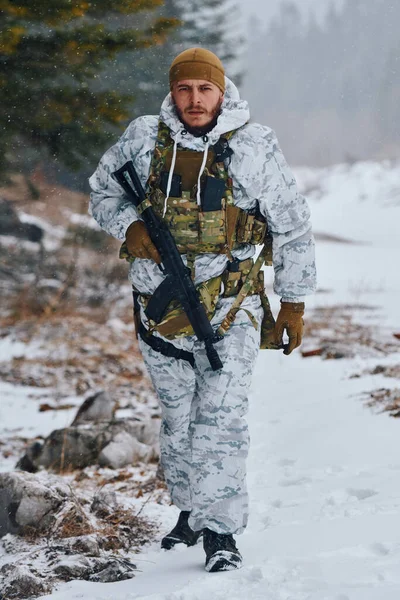 Beyaz kışlık kamuflaj ve taktik yelek giyen silahlı bir asker karlı bir orman yolunda yürüyor. Kararlı ifadeler ve nefesler soğuk havada görülebiliyor. Dayanıklılık, odaklanma ve askeriyede görülebilir.