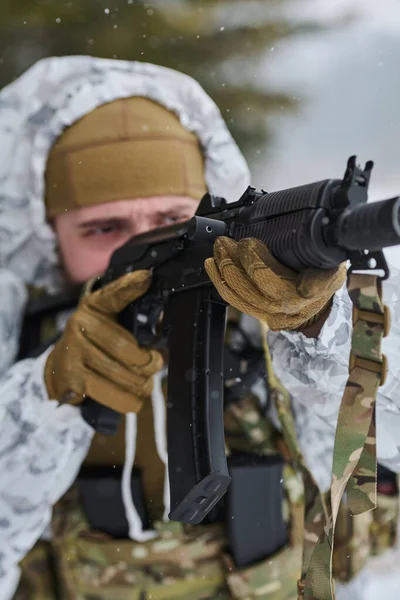Beyaz kış kamuflajlı silahlı asker, soğuk hava askeri operasyonları ve muharebe hazırlıklarında odaklanma, hazırlık ve taktik disiplin gösteren karlı alan eğitimi sırasında bir saldırı tüfeğini hedefliyor..