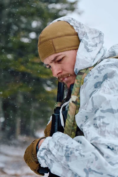Beyaz kış kamuflajı takan odaklanmış bir asker ve bronz bir bere, ormanda kar yağarken tüfeğini ve teçhizatını ayarlıyor, konsantrasyon, hazırlık ve soğuk hava askeri eğitimlerini iletiyor..