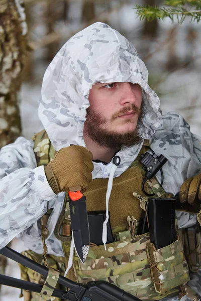 Beyaz kışlık kamuflaj başlığı ve taktik plaka taşıyan silahlı bir asker, karlı bir ormanda devriye gezerken bıçağını tutuyor, hazırlık, hayatta kalma ve askeri operasyonları sürdürüyor..