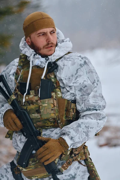 Beyaz kış kamuflajı ve taktiksel yelek giyen silahlı asker kar yağarken tetikte, karlı bir dağ manzarasını tararken veya soğuk hava askeri operasyonları sırasında tüfeği kavrıyor.