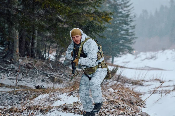 Beyaz kış kamuflajlı ve taktik teçhizatlı bir asker, karlı bir ormanda tüfekle ihtiyatlı bir şekilde ilerler. Düşen kar ve soluk renkler soğuk, ihtiyatlı, hazırlıklılık ve açık hava ordusunu taşır.