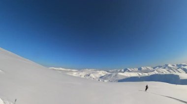 Tek başına bir maceracı uçsuz bucaksız bir dağ yamacındaki taze toz karları oyar. Heyecan verici bir helikopter kayağı ve açık mavi gökyüzü altında serbest gezinti sırasında..