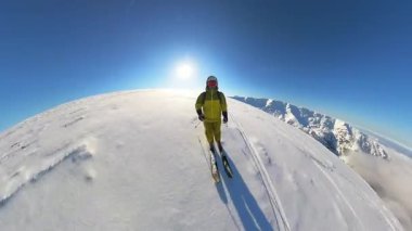 Helikopter kayağı macerasının heyecanını yaşayın. Bir serbest kayakçı görkemli bir dağın tepesinde duruyor. Etrafı, parlak mavi bir gökyüzünün altında geniş, taze ve derin toz karla kaplı.