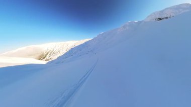 Deneyimli bir kıdemli kayakçı, uçsuz bucaksız bir dağ manzarasında coşkulu bir helikopter kayağı ve serbest gezinti sırasında el değmemiş, derin toz karda taze izler bırakır. Neşe ve özgürlüğü vurguluyor.